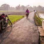 Murshidabad, West Bengal, India - January 2018: A man sitting with his bicycle on a rural road running through green fields in the district of Murshidabad.